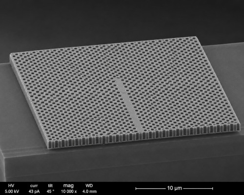 Scanning electron microscope style image of a two-dimensional photonic crystal consisting of a periodic array of air holes etched into a dielectric slab, illustrating the type of structure commonly used to control and guide light